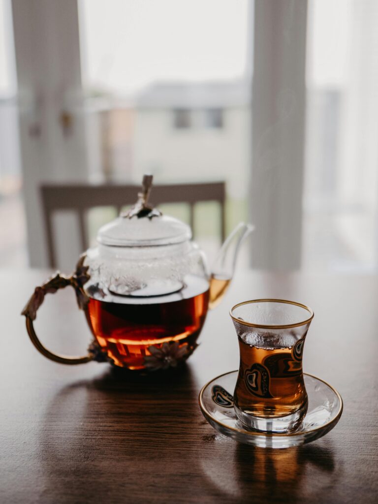 A cozy indoor setting features a steaming glass teapot with Turkish tea glass on a wooden table by the window.