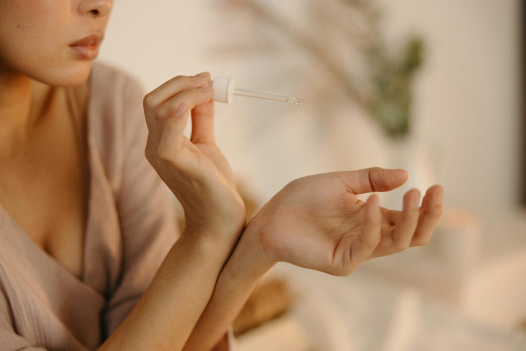 A woman applying serum on her wrist in a cozy home setting.